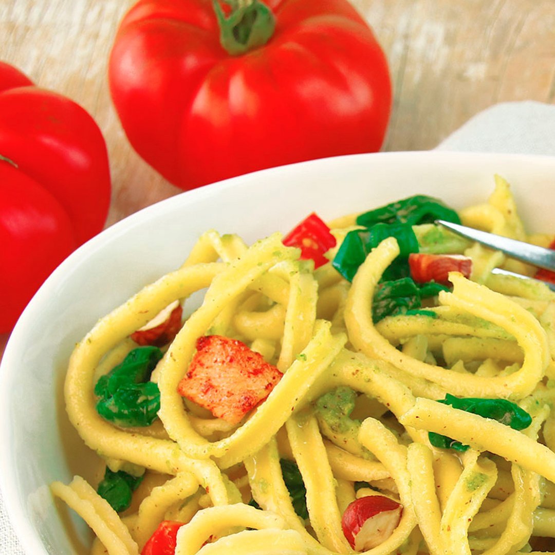 Spaetzle pasta with spinach pesto, cherry tomatoes, and pieces of chicken in a white bowl