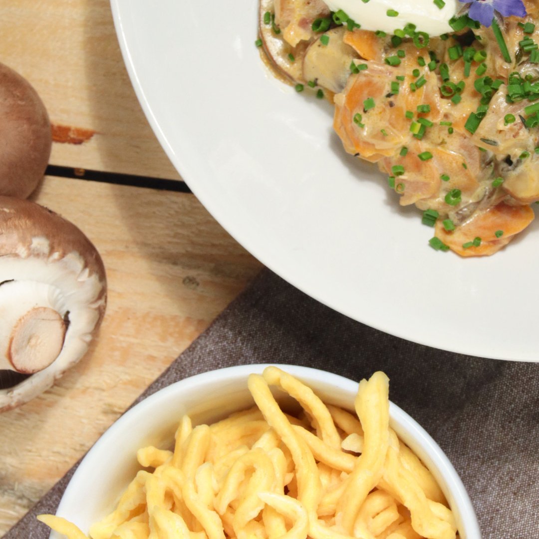 Carrot and mushroom 'Geschnetzeltes' dish garnished with herbs, served with a side of golden fries and fresh mushrooms on a wooden table