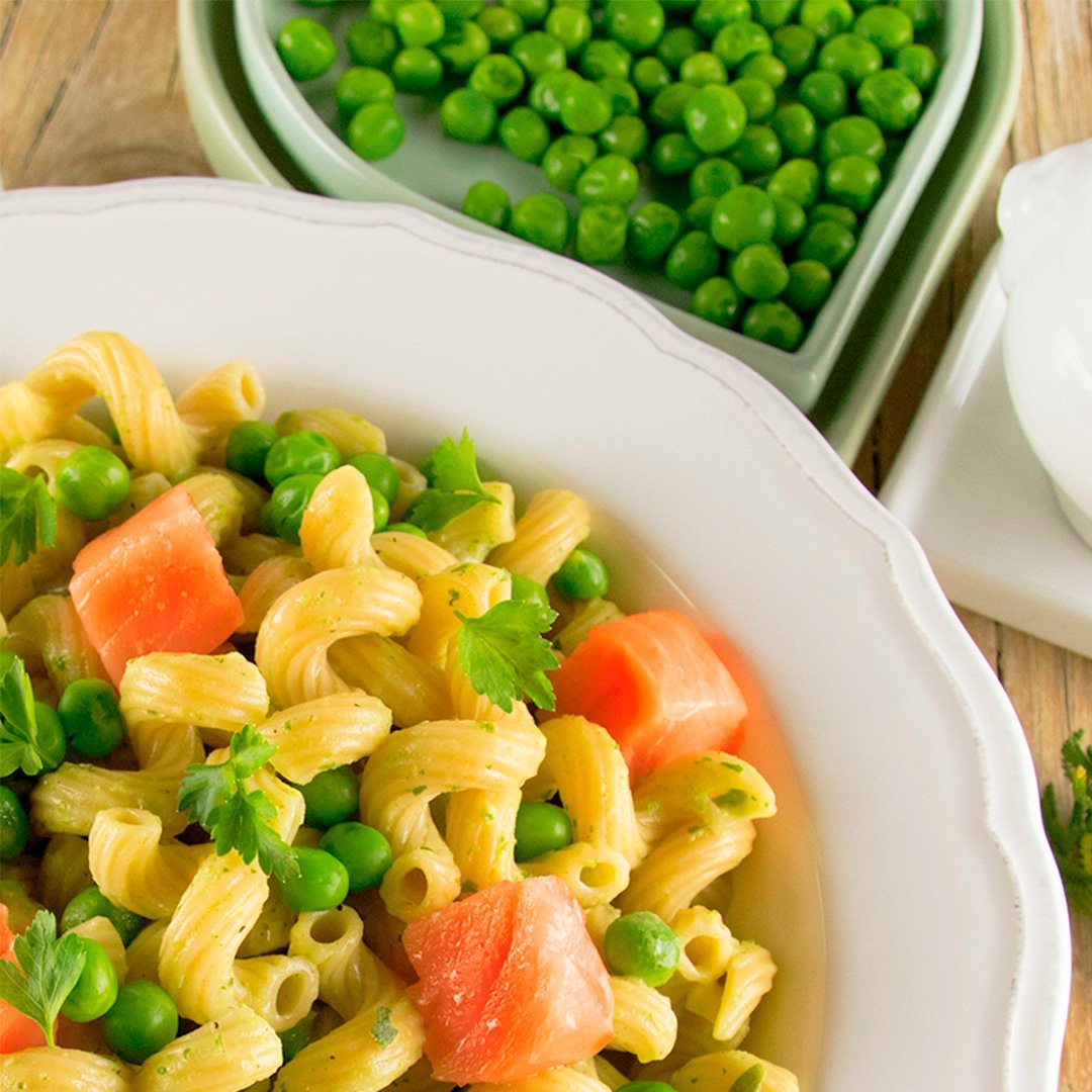 Corkscrew pasta with green pea sauce and pieces of salmon in a white bowl, with a side dish of green peas in the background