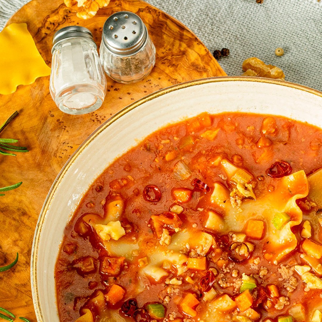 Bowl of mini-lasagne-soup with walnut bolognese, garnished with herbs, salt and pepper shakers on a yellow cloth