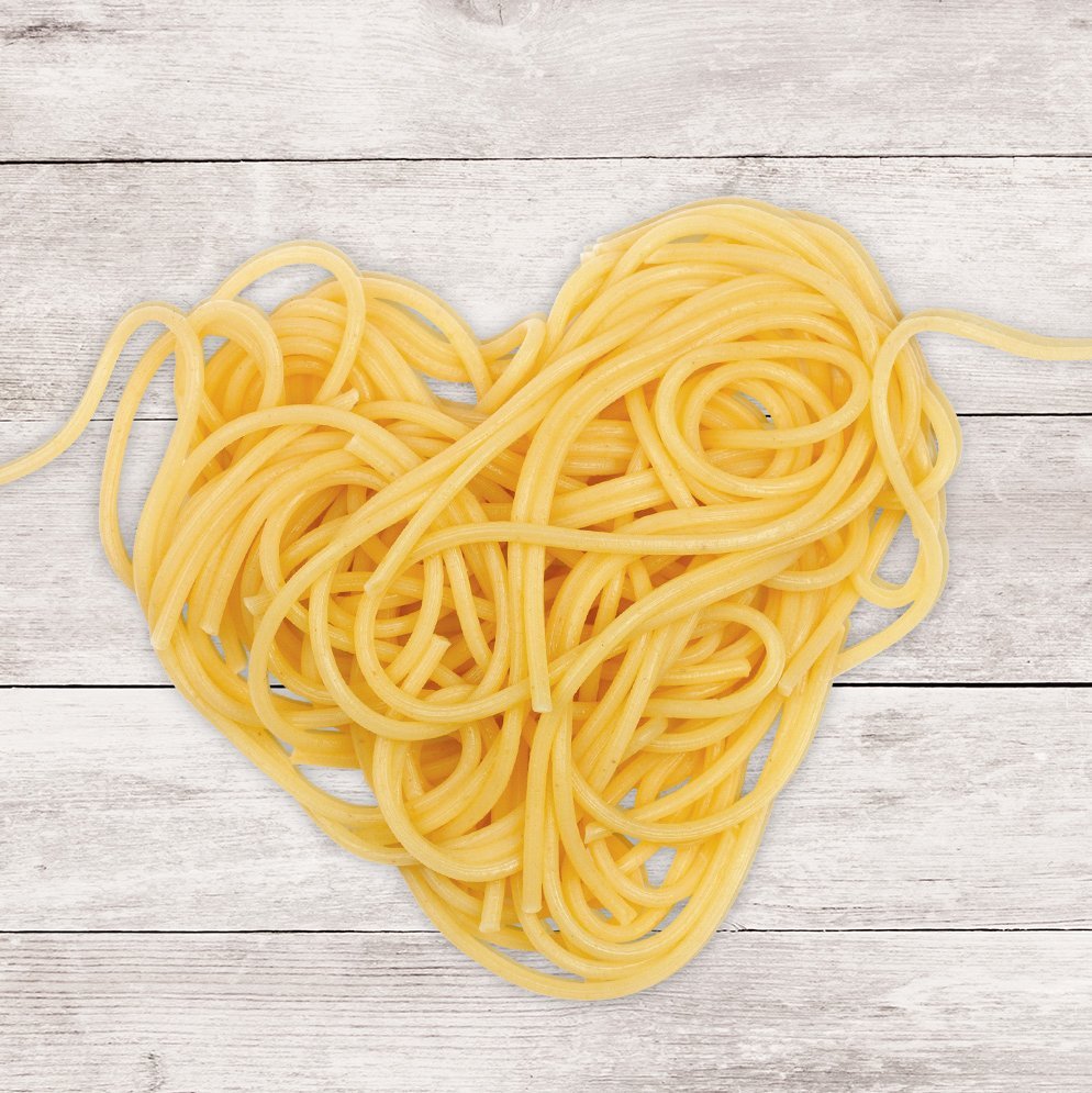 Ein Nudelherz aus Spaghetti auf einer Holzplatte.