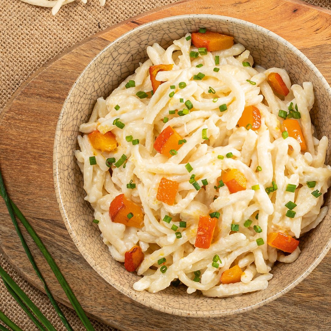 Bowl of pumpkin cheese spaetzle garnished with chopped herbs on a woven placemat