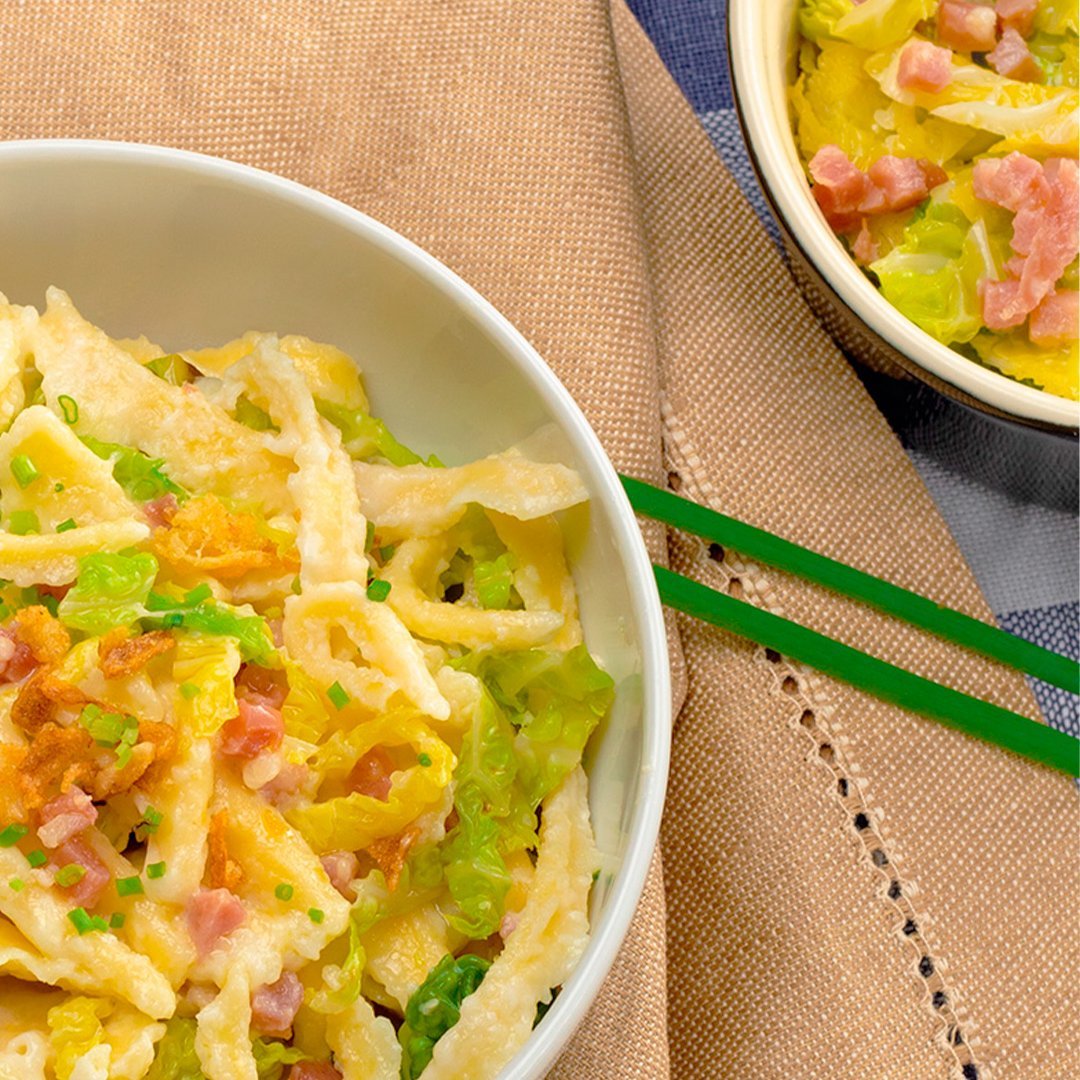 Savoy cabbage and cheese spaetzle served in white bowls with green chopsticks on a beige cloth
