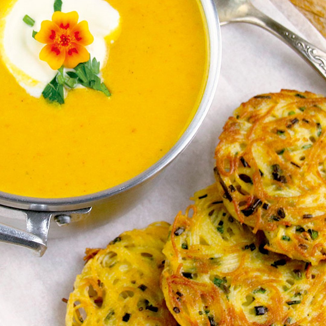 Bowl of creamy pumpkin soup garnished with herbs, served with golden-brown pasta fritters on the side