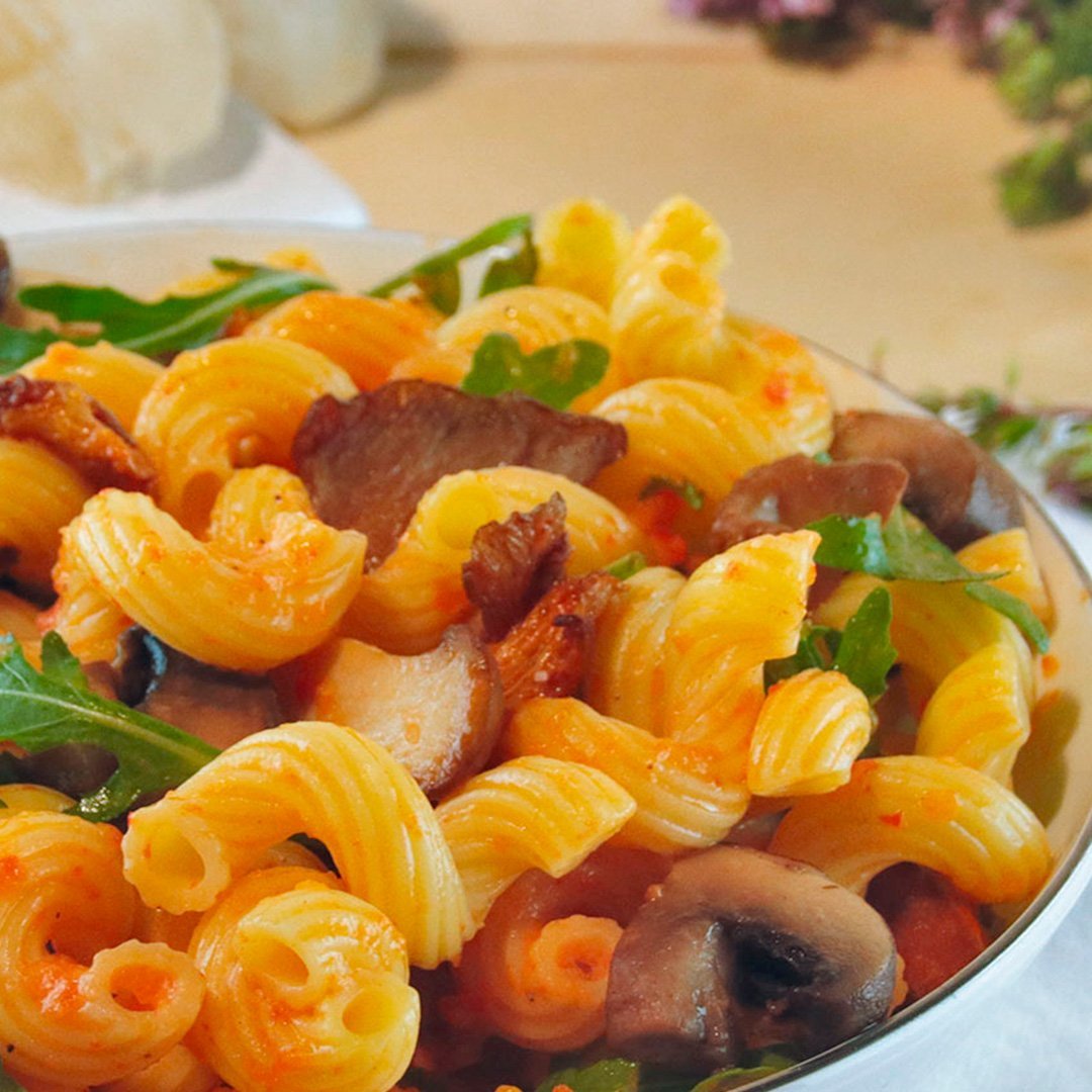 Bowl of lukewarm corkscrew pasta salad with mushrooms and greens