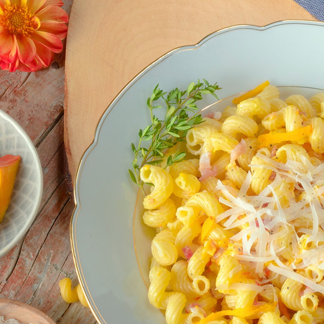 Corkscrew pasta topped with creamy pumpkin-bacon sauce and grated cheese on a light blue plate, garnished with fresh herbs