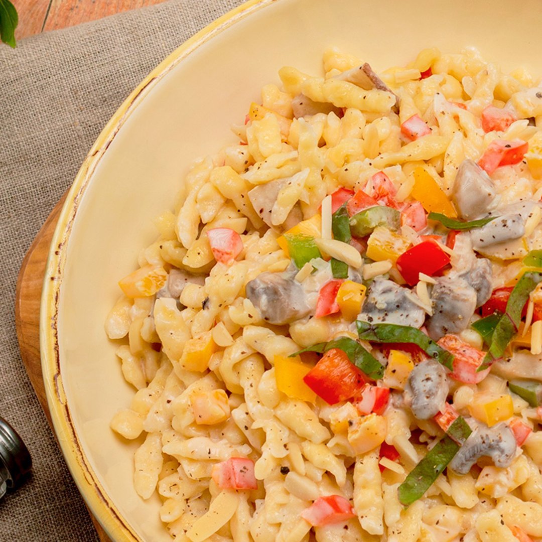 Homestyle spaetzle pasta mixed with diced red and green bell peppers, garnished with herbs on a beige plate